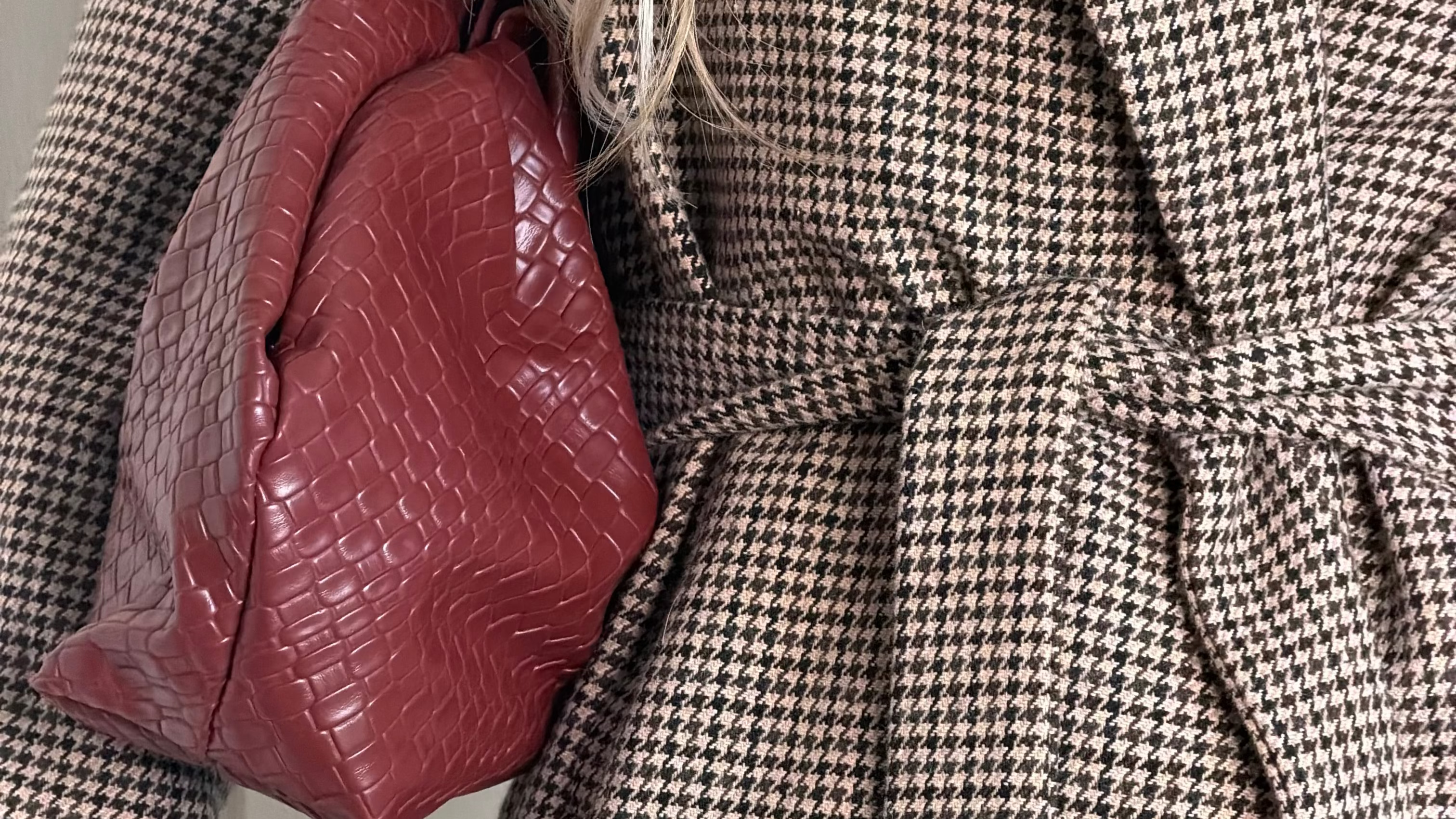 Close-up of a houndstooth blazer styled with a burgundy textured handbag.